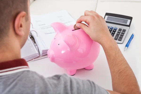 Rear view of young man putting coin into piggy bank — Stock Photo, Image