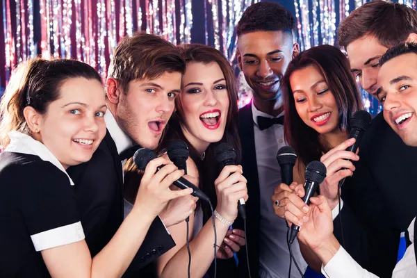 Amigos cantando em microfones na festa de karaoke — Fotografia de Stock