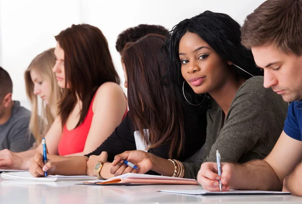 Étudiant confiant assis avec des camarades de classe écrivant au bureau — Photo