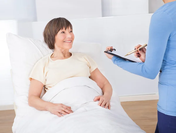 Cuidador con portapapeles atendiendo a la mujer mayor — Foto de Stock