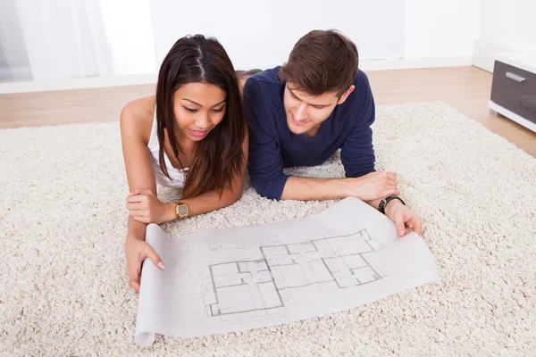 Pareja mirando el plano mientras está sentado en la alfombra — Foto de Stock