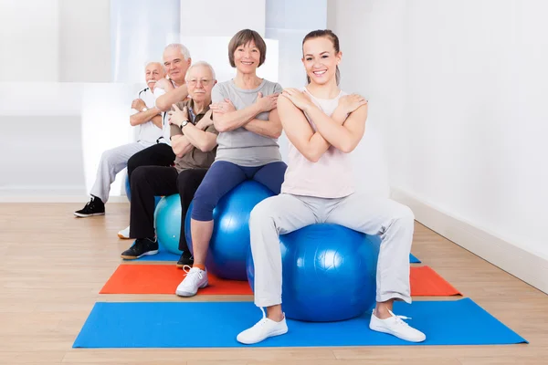 Trainer und Senioren sitzen auf Fitnessbällen — Stockfoto