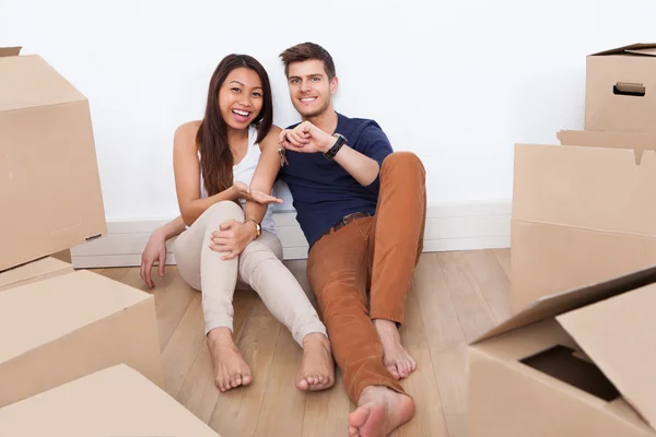 Paar sitzt auf dem Boden und hält Schlüssel aus dem neuen Zuhause in der Hand — Stockfoto