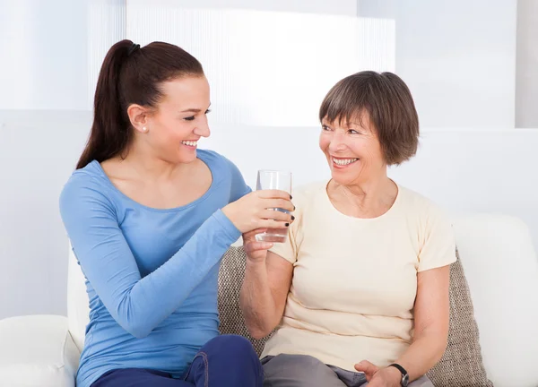 Opiekun daje szklankę wody do starszych kobiety — Zdjęcie stockowe
