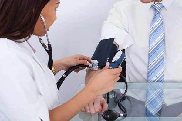 Médico revisando la presión arterial del empresario — Foto de Stock