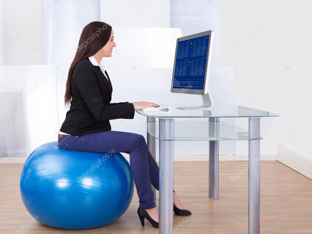 Businesswoman Using Computer While Sitting On Pilates Ball