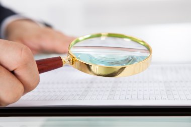 Businessman Examining Audit With Magnifying Glass In Office