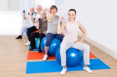 fitness topları üzerinde otururken el ağırlıkları kullanan kişiler