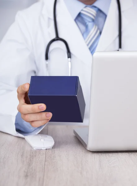 Arzt hält Medikamentenbox mit Laptop in der Hand — Stockfoto