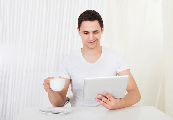 Hombre usando tableta digital mientras toma café en la mesa de comedor —  Fotos de Stock