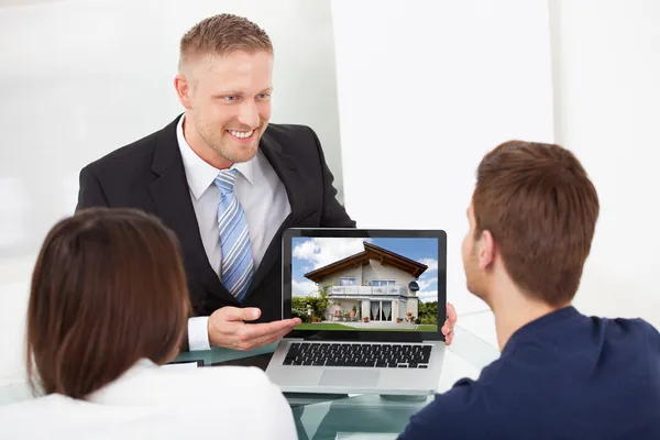 Advisor mostrando a imagem da casa ao par no portátil — Fotografia de Stock