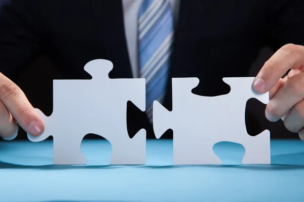 Businessman Joining Puzzle Pieces At Desk — Stock Photo, Image