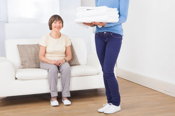 Vicevært Bærer Håndklæder med Senior Woman Sitting On Sofa - Stock-foto