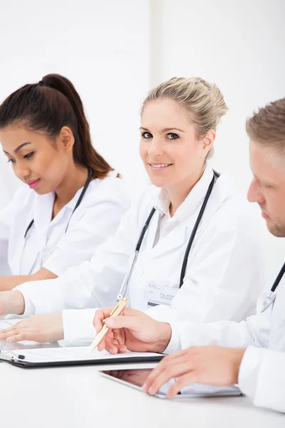 Row Of Doctors Writing At Desk — Stock Photo, Image