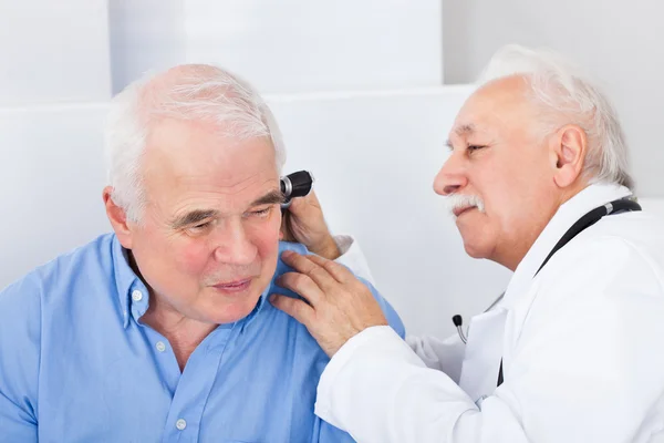 Доктор осматривает ухо пожилого человека с помощью отоскопа — стоковое фото