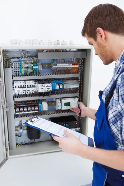 Technicus bedrijf Klembord terwijl onderzoeken fusebox — Stockfoto