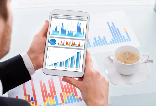 Geschäftsmann vergleicht Grafiken auf digitalem Tablet am Schreibtisch — Stockfoto