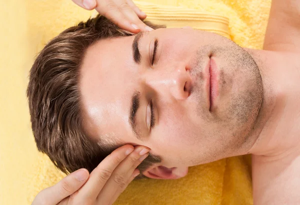 Розслаблений чоловік приймає масаж лоба в спа — стокове фото