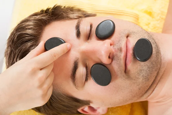 Человек, получающий каменную терапию на лице в спа — стоковое фото