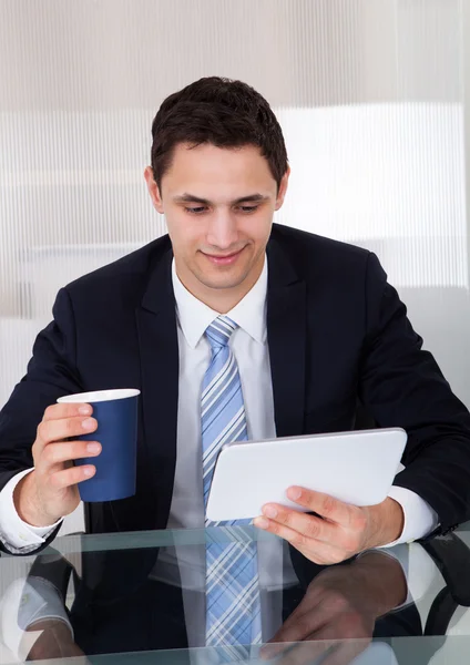 Бизнесмен с помощью цифровой таблетки во время питья кофе в офисе — стоковое фото