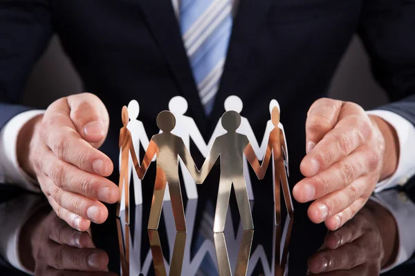 Businessman's Hands Protecting Team Of Paper People On Desk — Stock Photo, Image