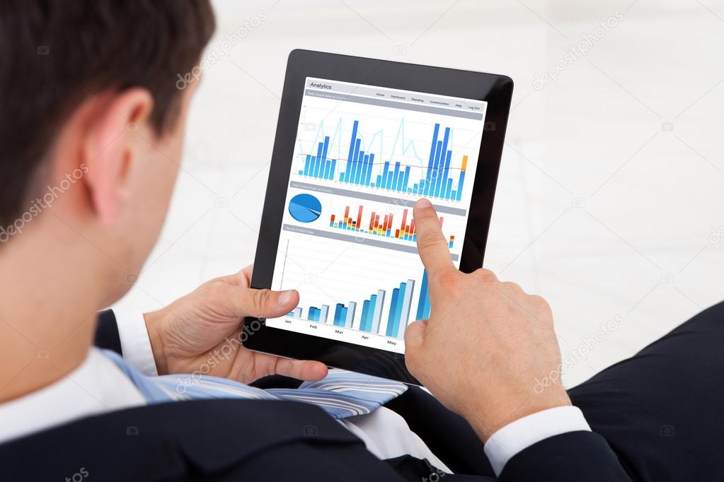 Businessman Comparing Graphs On Digital Tablet In Office