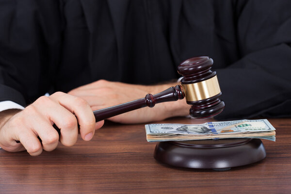 Судья стучит молотком по банкнотам

