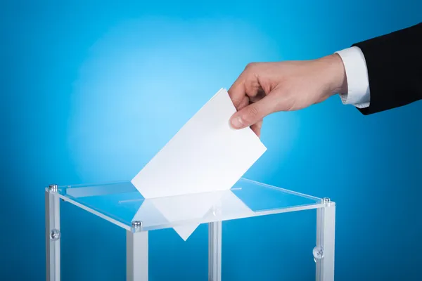 Бизнесмен кладет бумагу в избирательный ящик — стоковое фото