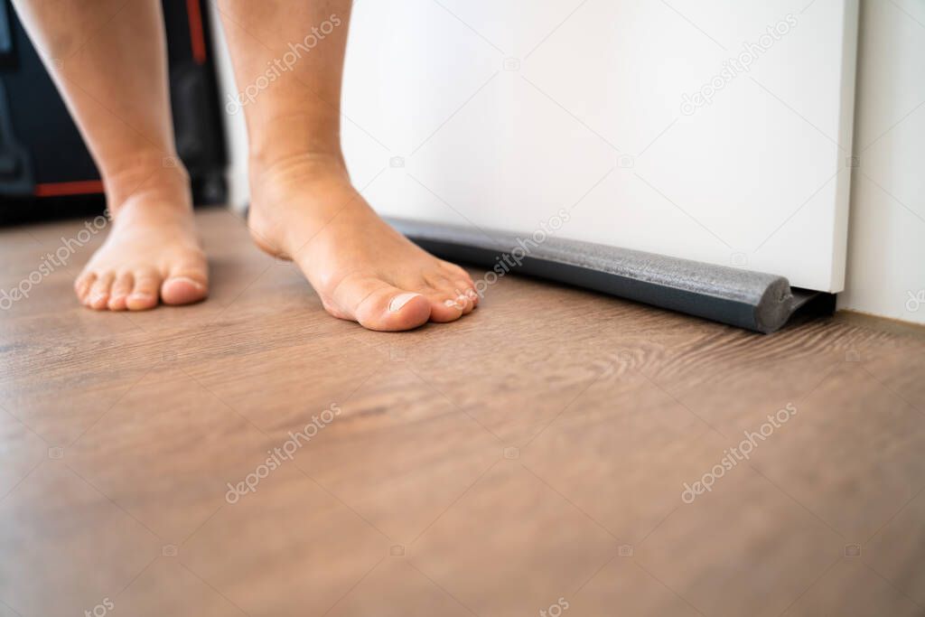 Person Walking Barefoot Near Draft Excluder Under Door Blocking Cold Air From Traveling Around