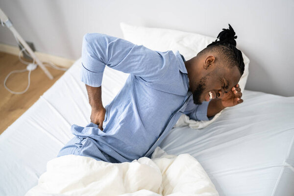 Man Suffering From Back Pain Sitting On Bed