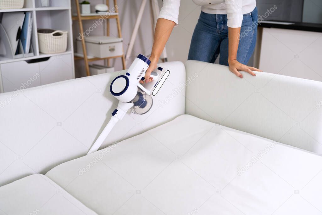 Young Female Worker Cleaning Sofa With Vacuum Cleaner