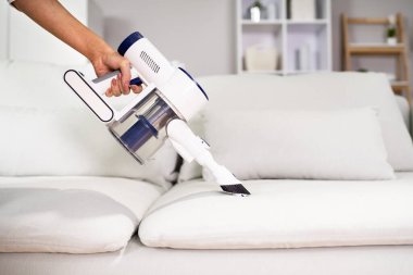 Genç Bayan İşçi Elektrikli süpürgeyle kanepeyi temizliyor.