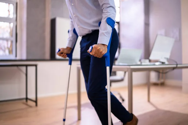 職場やオフィスで松葉杖を持つ労働者 ハンディキャップリハビリテーションの利点 — ストック写真