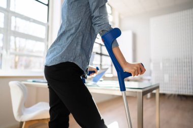 İş yerinde ya da ofiste koltuk değnekleriyle çalışan bir işçi. Engelli Rehabilitasyon Yararları