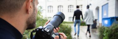 Genç Paparazzi Fotoğrafçısı şüpheli bir şekilde bir çiftin birlikte yürüdüğü bir fotoğraf çekiyor.