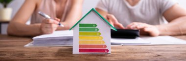 Ahşap Masa Üzerinde Hesap Makinesi kullanarak Mutlu Çift Önünde Enerji Verimliliği Oranı Gösteren Ev