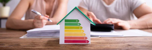 Dom Pokazuje Wskaźnik Efektywności Energetycznej Przed Szczęśliwą Parą Pomocą Kalkulatora — Zdjęcie stockowe