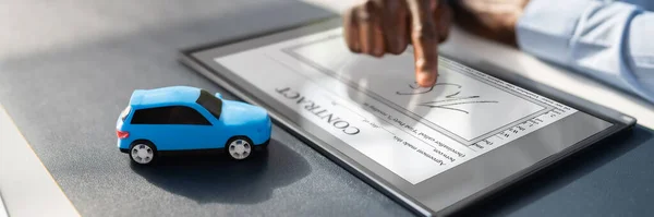 A Person\'s Hand Signing Car Loan Agreement Contract With Car Toy On Glass Desk