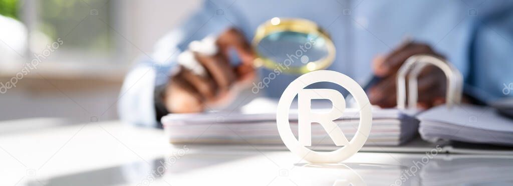 Close-up Of White Registered Trademark Sign Near Documents Over Desk