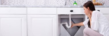 Mutfak lavabo borudan su kaçağı durdurmaya çalışan bir kadının arkadan görünüş