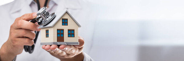 Крупный план руки врача, осматривающего модель дома со стетоскопом
