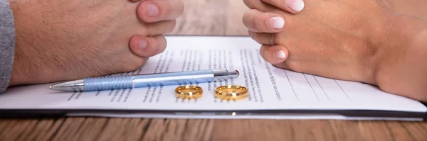 Hand Des Ehepaares Mit Scheidungsvertrag Und Goldenen Eheringen Auf Holztisch — Stockfoto