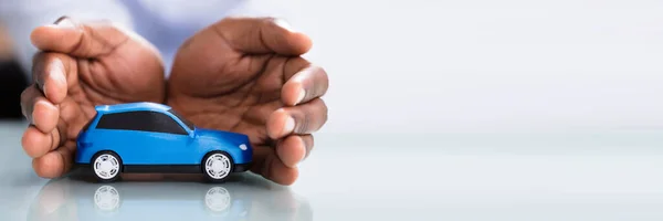 反射の机の上のブルーのおもちゃの車を保護する実業家の手 — ストック写真