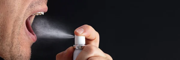 Close-up Of Man Using Mouth Freshener Against Black Background