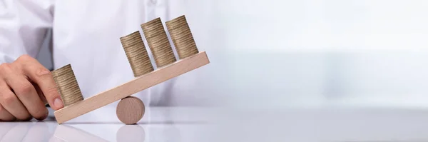 木製シーソーに積み上げコインのアンバランスを示す実業家の手 — ストック写真