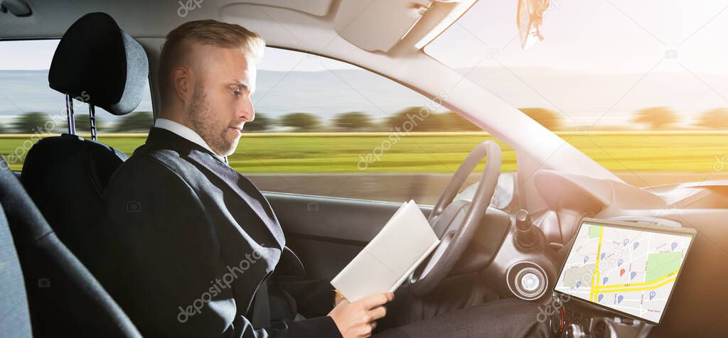 Young Businessman Sitting Inside Self Driving Car And Reading Book
