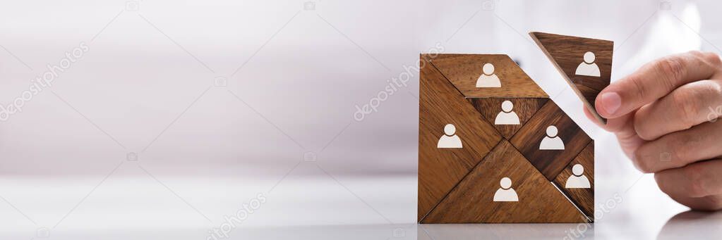 Businessman's hand building tangram square block with human figures