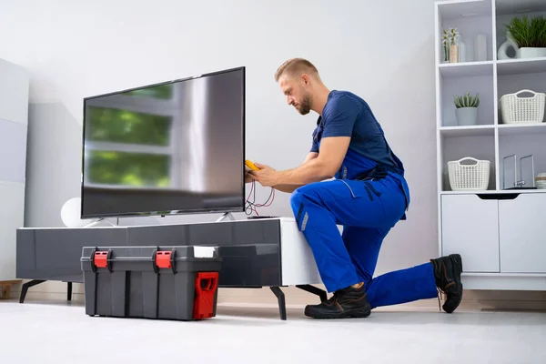 Male Technician Repairing Television With Digital Multimeter At Home