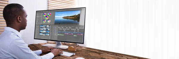 An African American Businessman Editing The Video On Computer Over The Wooden Desk