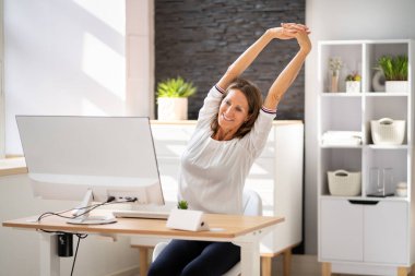Kadın büro masasında geriniyor. Sandalye üzerinde esneme egzersizi